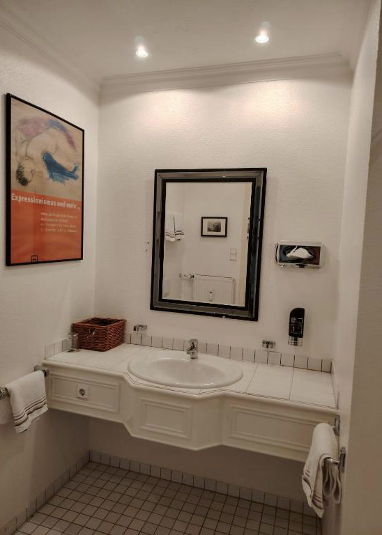 Helles Badezimmer mit weißem Waschtisch, großem Spiegel und Kunstplakat an der Wand