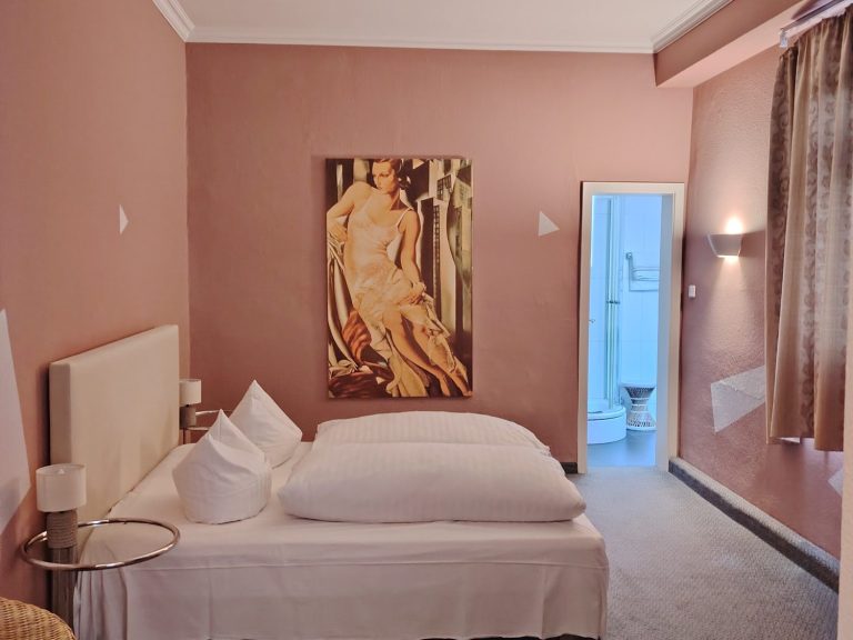 Zimmer in warmem Rosé mit Doppelbett, weißer Bettwäsche, großem Wandbild und Blick ins Bad